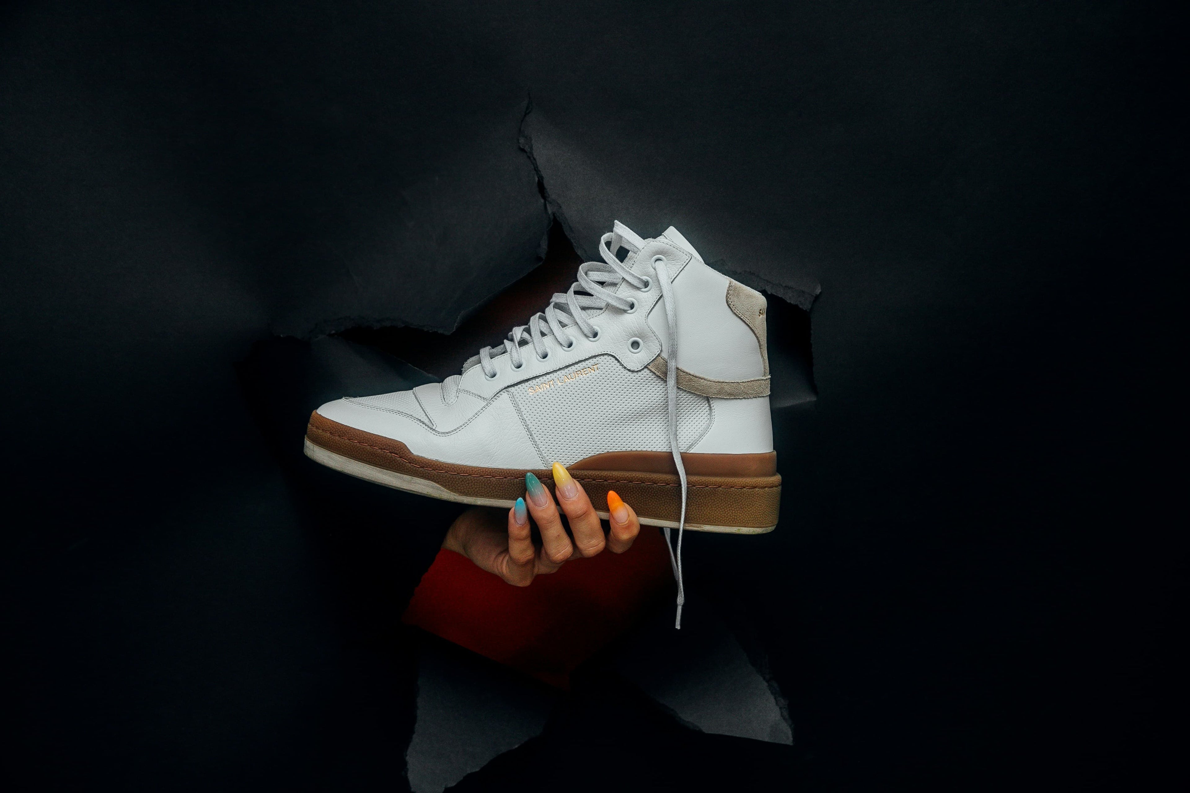 Weißer Damenschneaker wird durch ein Loch in der Wand gehalten